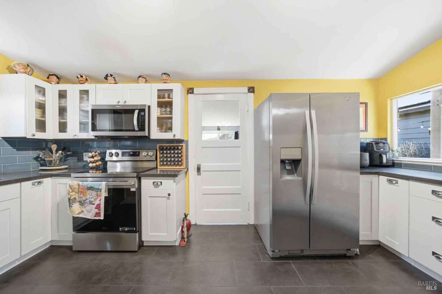 Kitchen with white cabinetry, stainless appliances, and a dark blue tile backsplash.