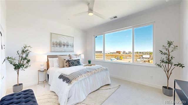 Staged bedroom with a white bed and large window overlooking low-rise buildings.