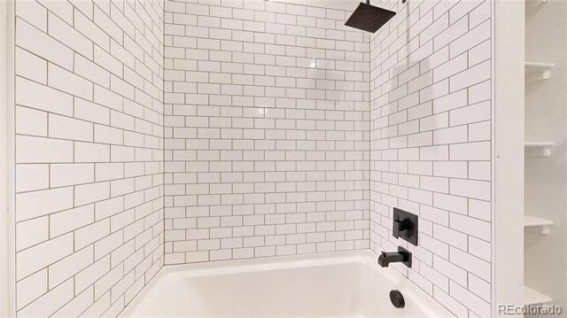 White subway-tile tub and shower with black fixtures and recessed shelves.