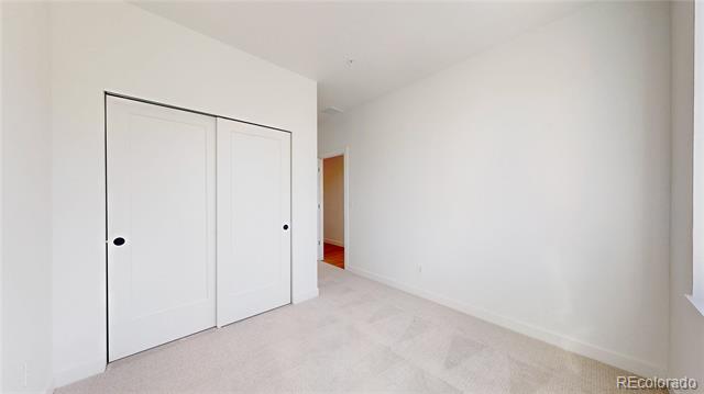 Empty carpeted bedroom with white sliding closet doors and an open doorway to the hall.