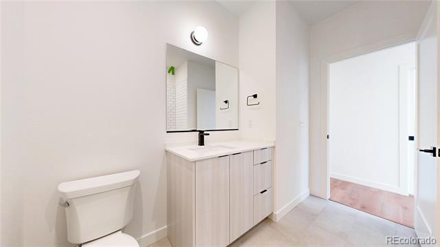 Bathroom with a light wood vanity, rectangular mirror, black faucet, and white toilet.