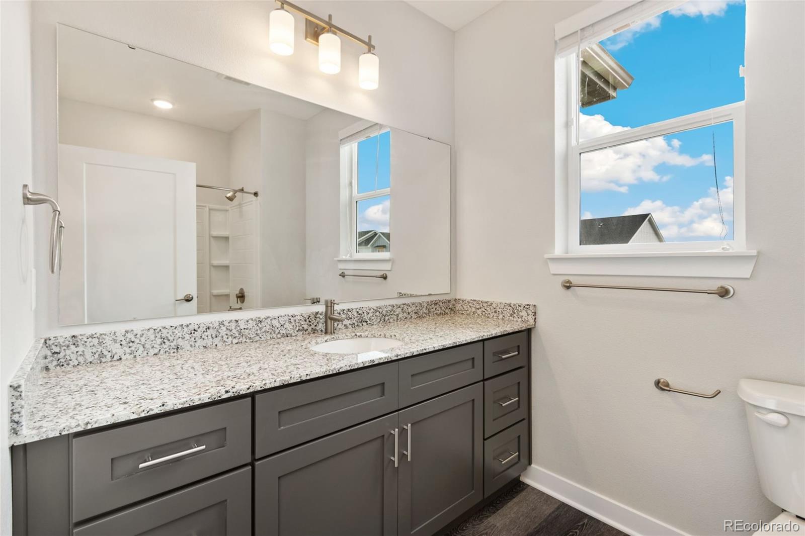 Bathroom with a gray vanity, speckled granite counter, large mirror, and tall sunny window.