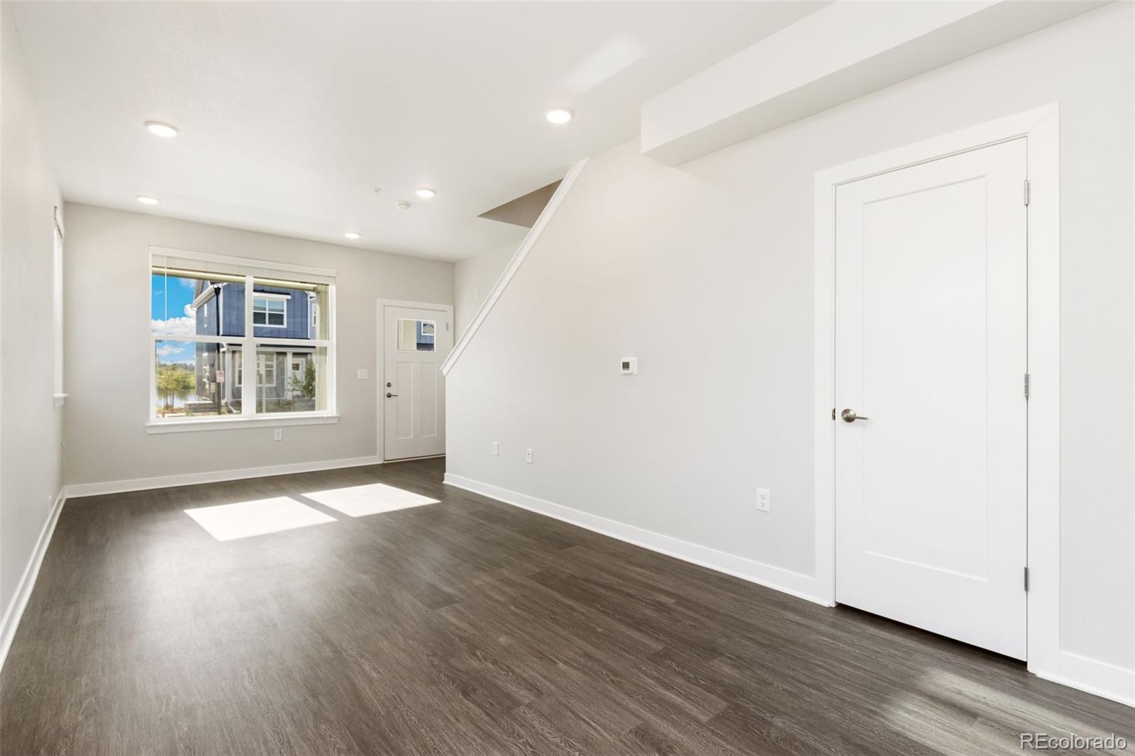 Vacant living area with dark flooring, a large window, and a staircase.