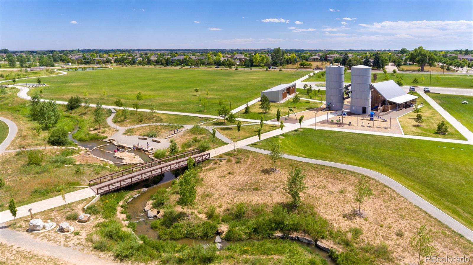 Neighborhood park with winding paths, a playground, and a pedestrian bridge over a creek.