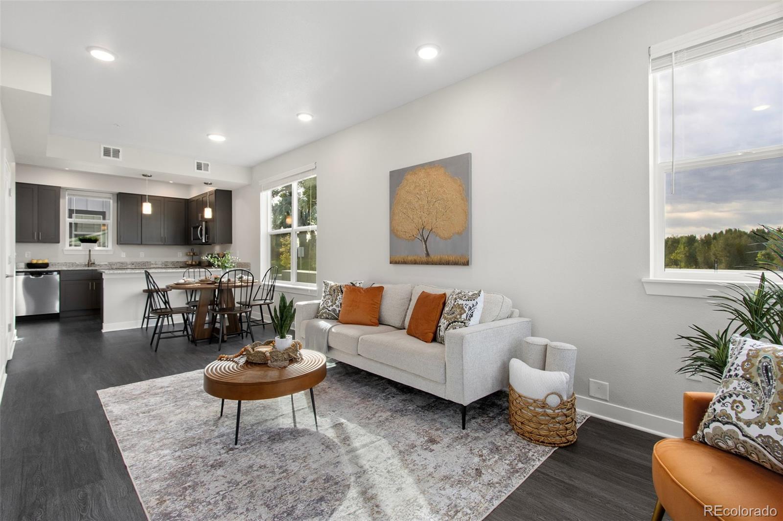 Open-plan living room with a white sofa, orange pillows, and adjoining kitchen and dining area.