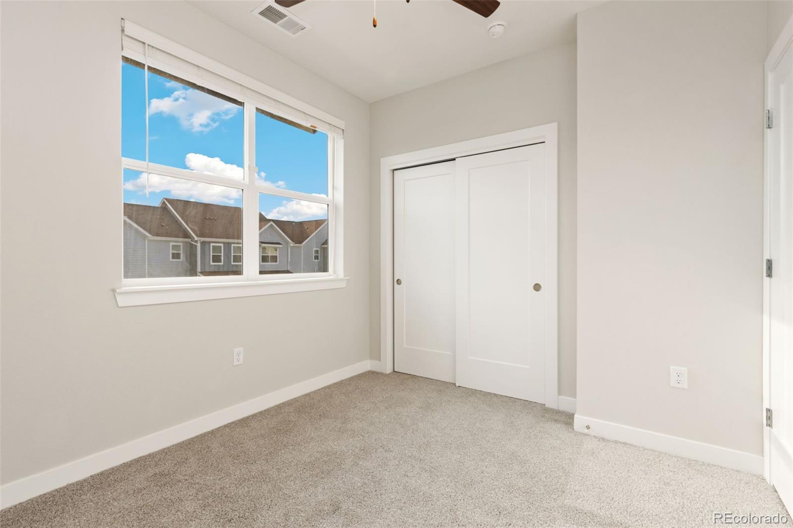 Empty bedroom with beige carpet, a large window, and a white sliding-door closet.