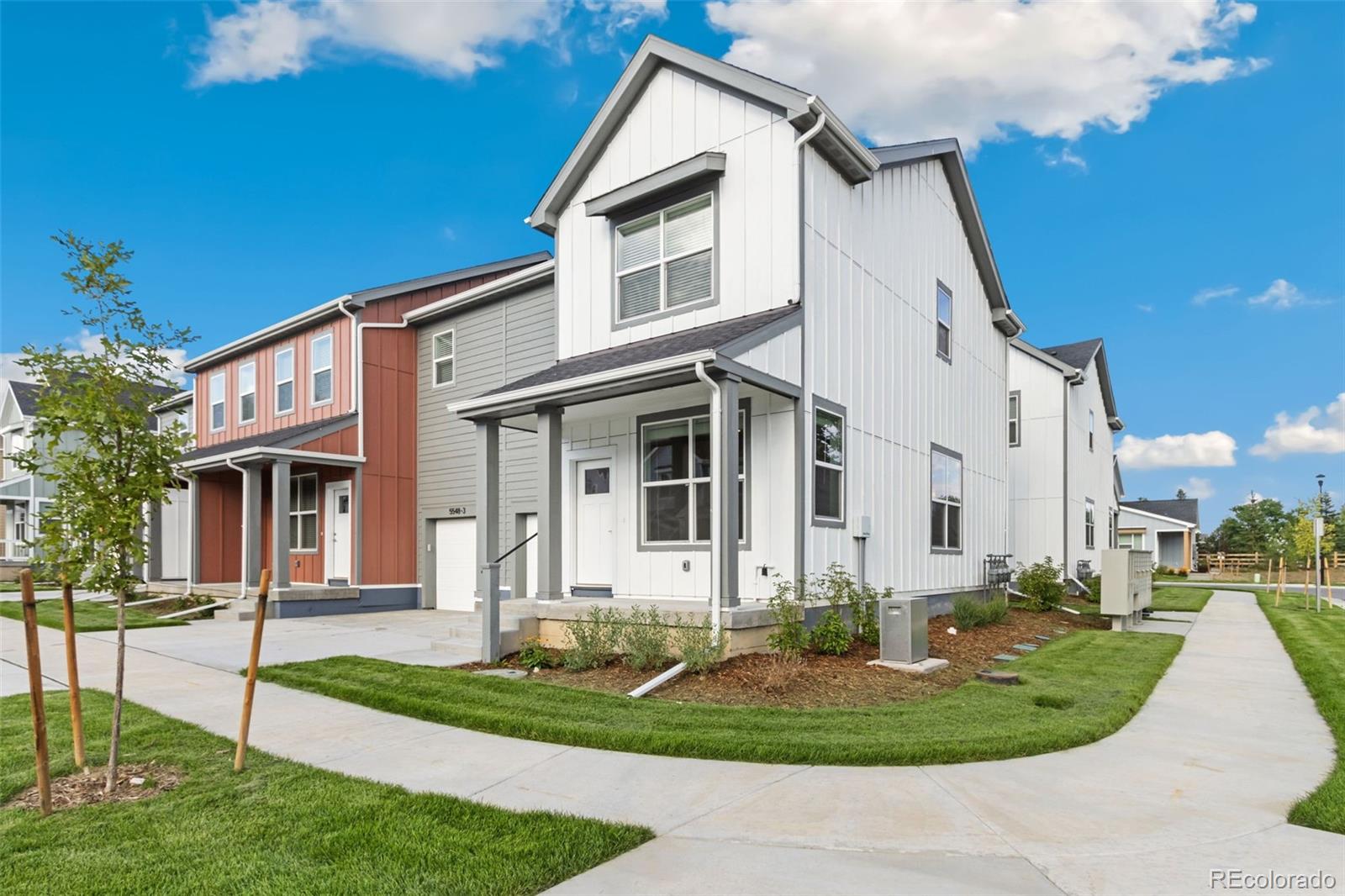 White two-story townhouse with a covered porch, driveway, and landscaped lawn.