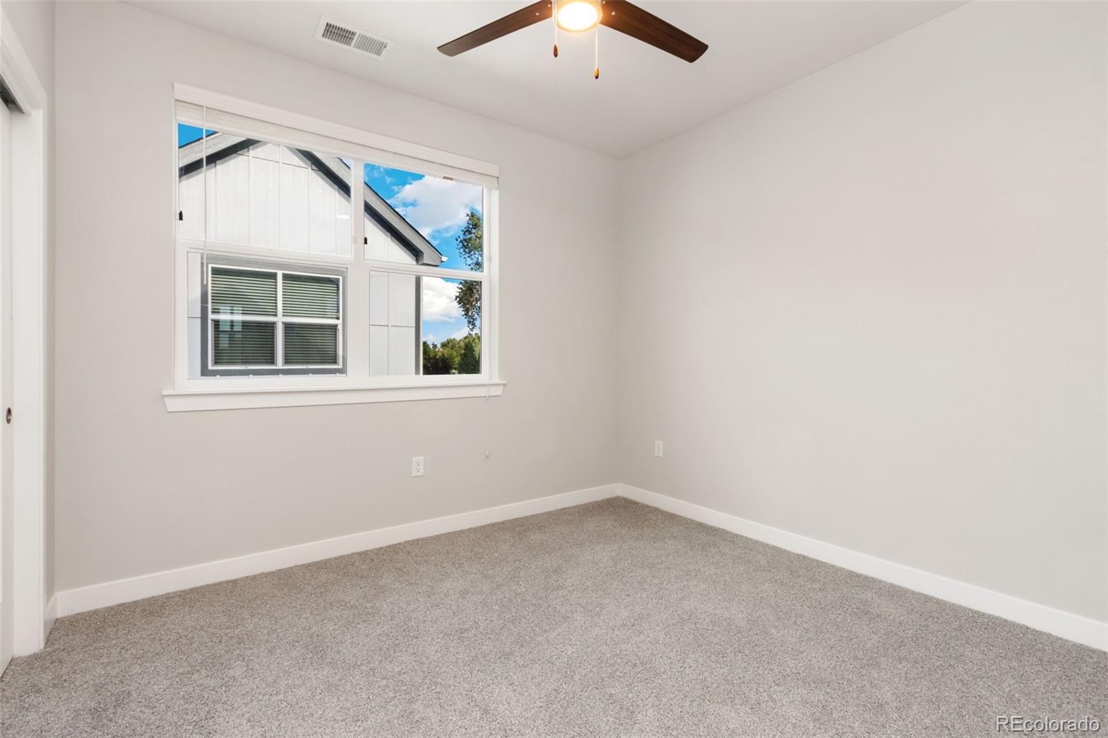 Empty bedroom with gray carpet, a large window, and a ceiling fan.