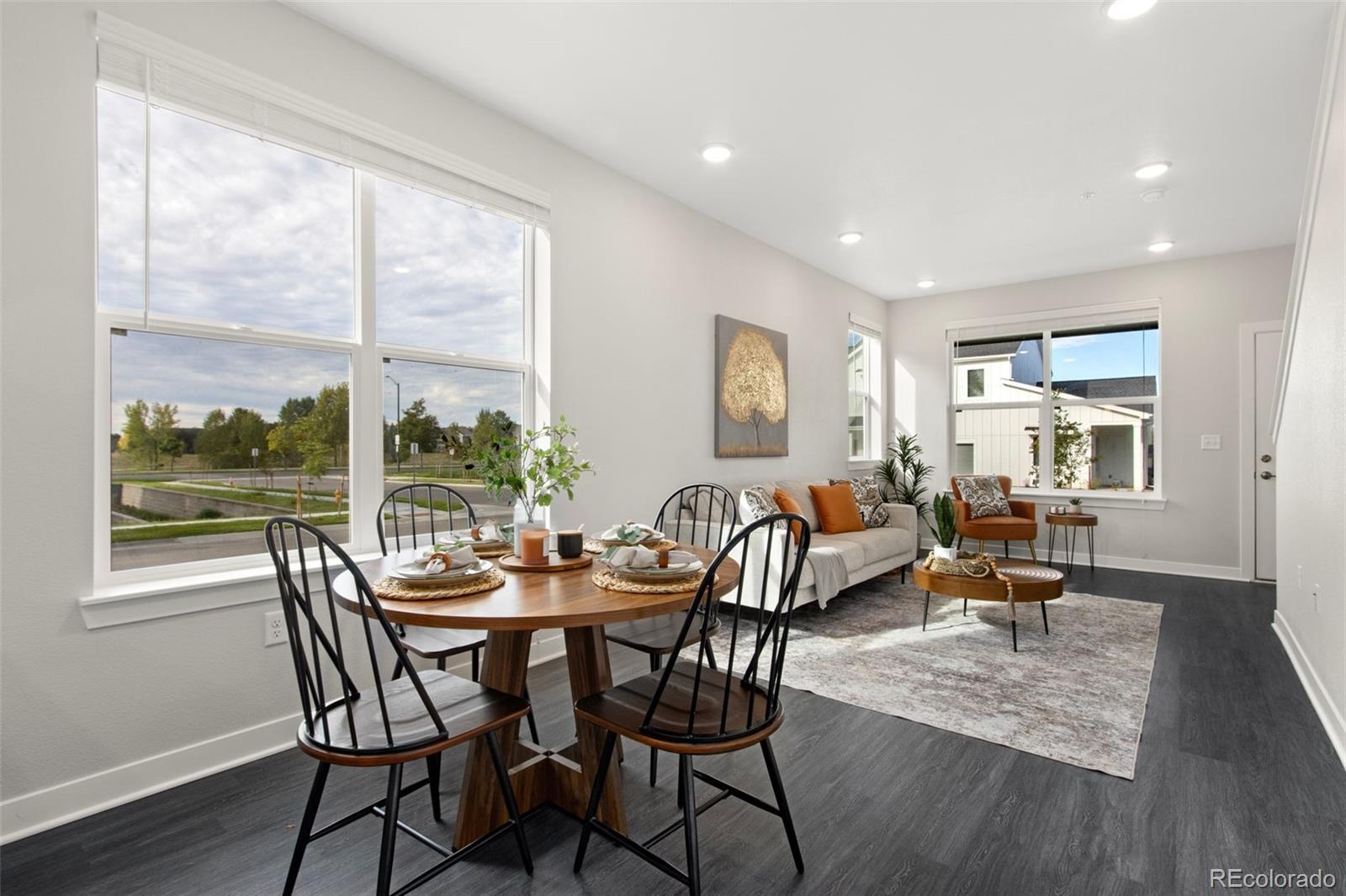 Open dining and living area with a round table, light sofa, and large windows.