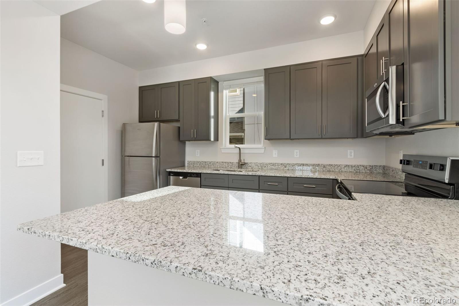 Kitchen with gray cabinets, stainless steel appliances, and a large granite island.