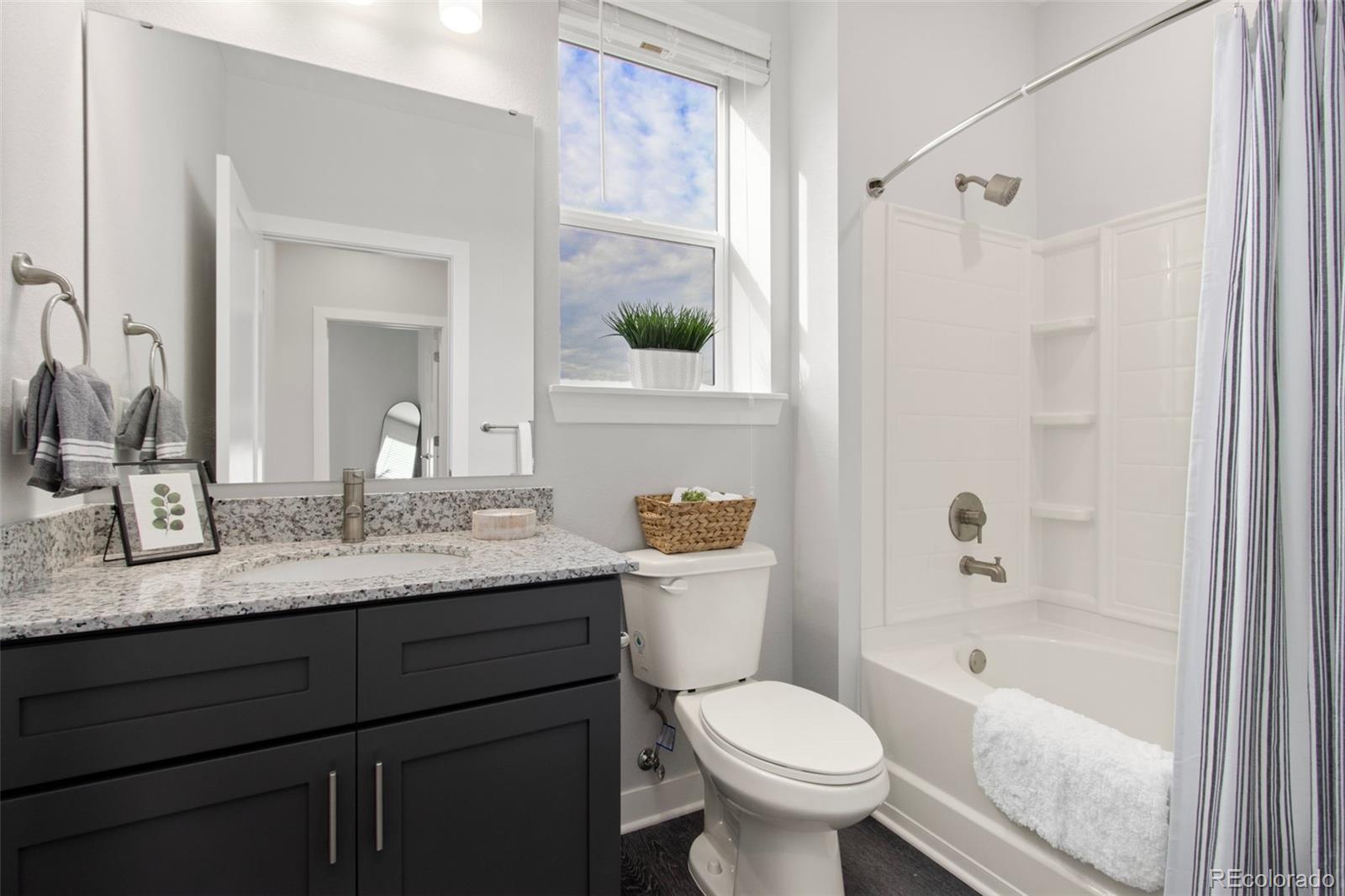 Bathroom with a dark vanity, stone countertop, and white tub-shower beside a tall window.