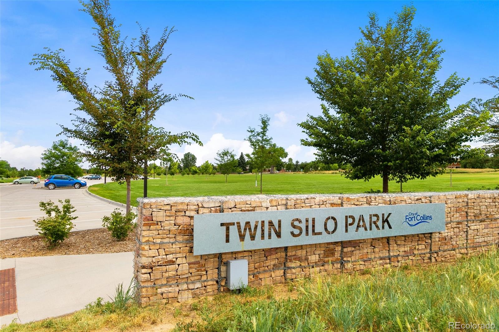 Twin Silo Park entrance sign beside a grassy lawn and parking area.