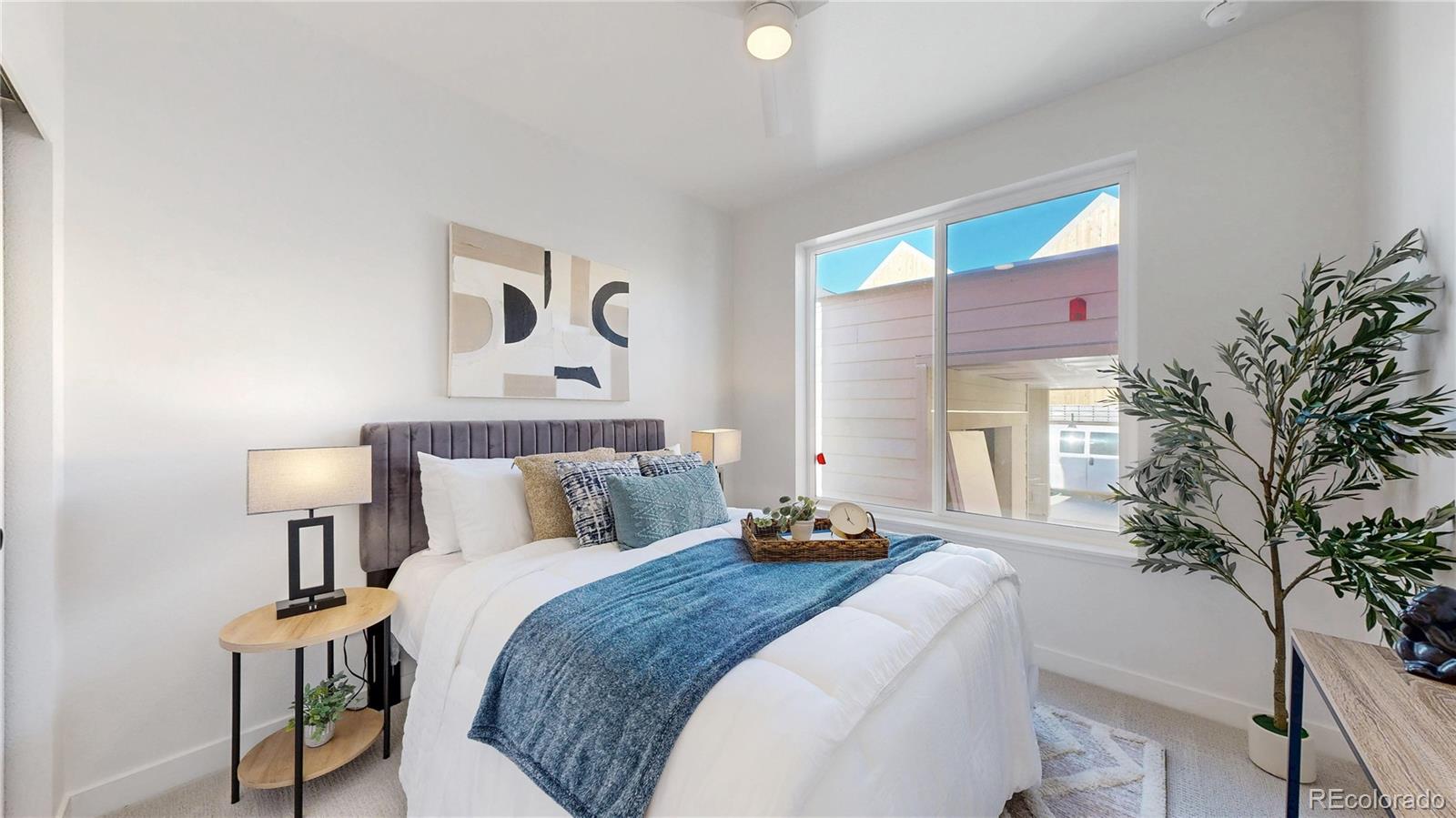 Staged bedroom with a white bed, blue throw, and large window.