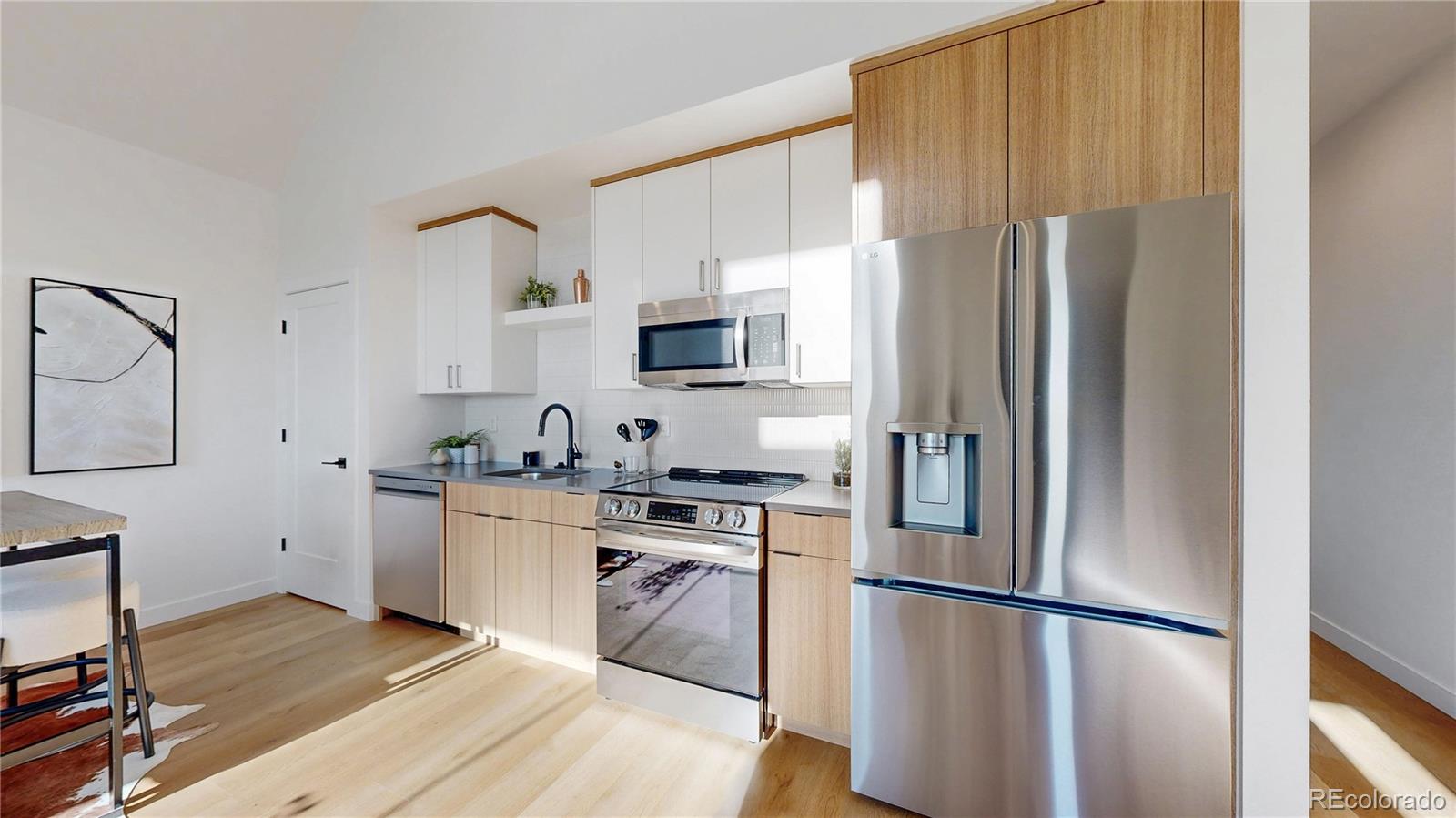 Modern kitchen with light wood cabinets, stainless steel appliances, and a large refrigerator.