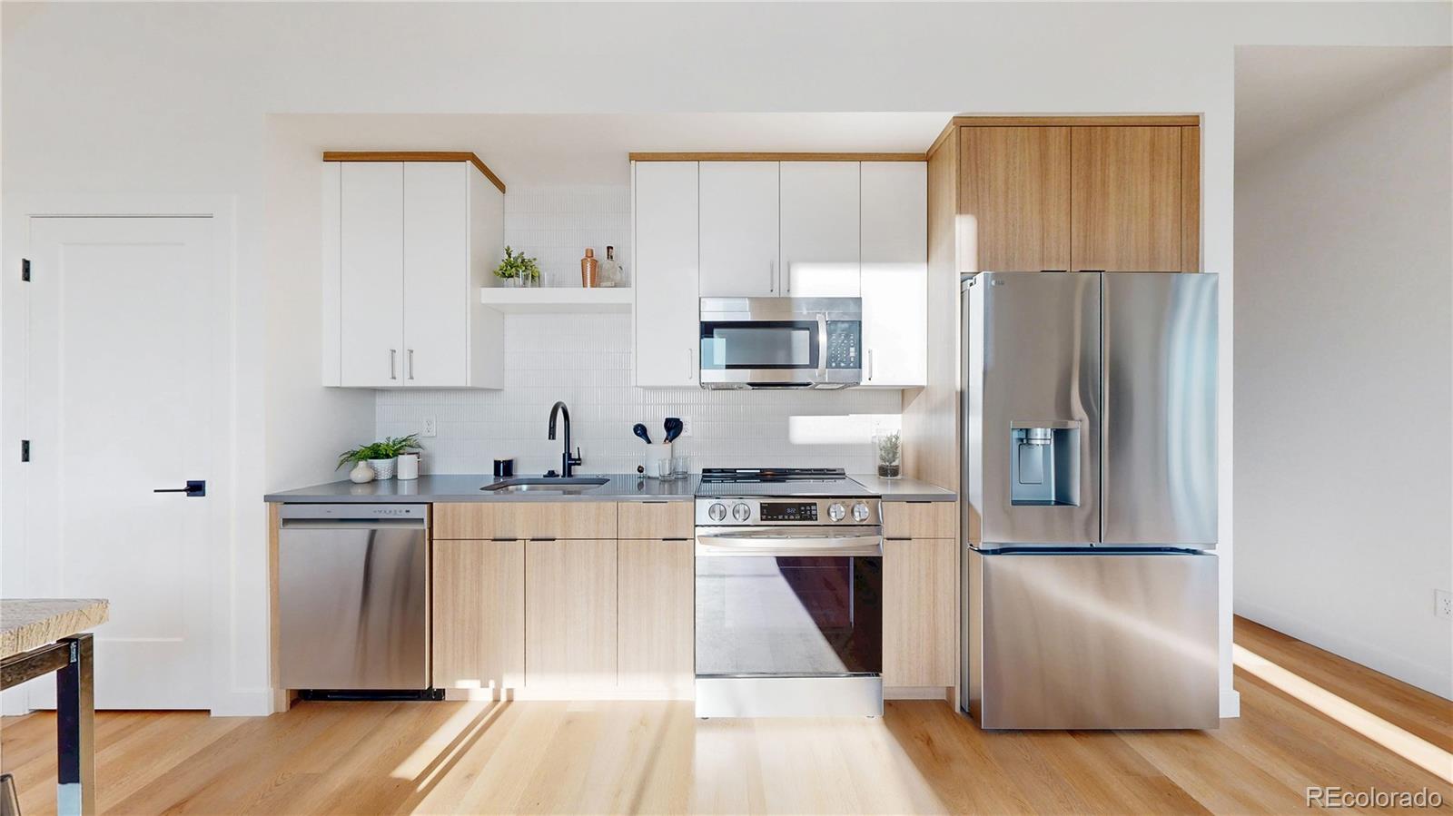Bright modern kitchen with white and wood cabinets, stainless steel appliances, and light wood floors.
