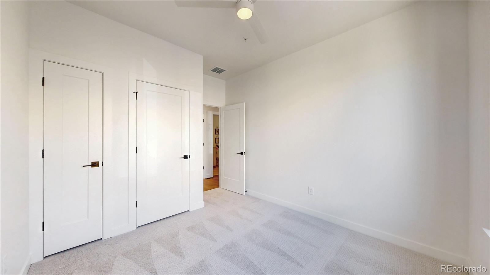 Empty carpeted bedroom with white paneled doors and a ceiling fan.