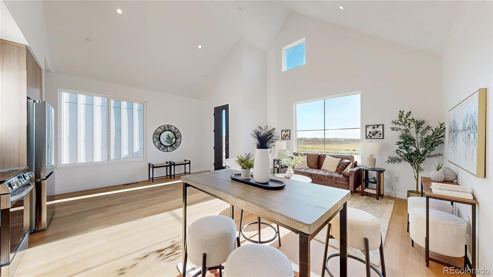 Open-plan living and dining area with vaulted ceilings, large windows, and a kitchen.