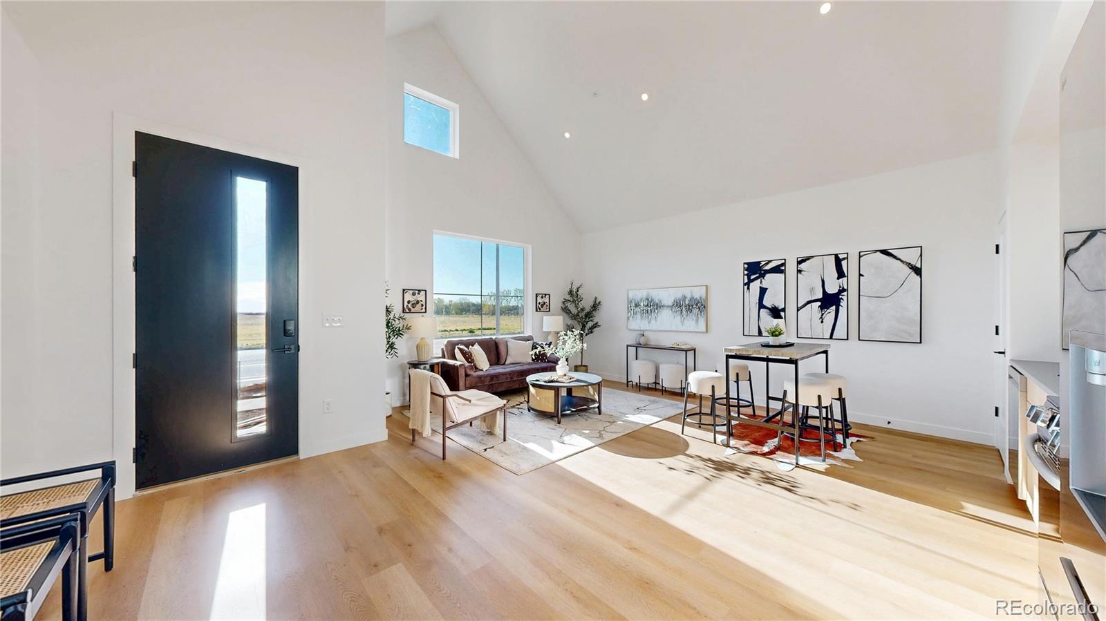 Staged open living and dining area with vaulted ceiling, large windows, and light wood floors.