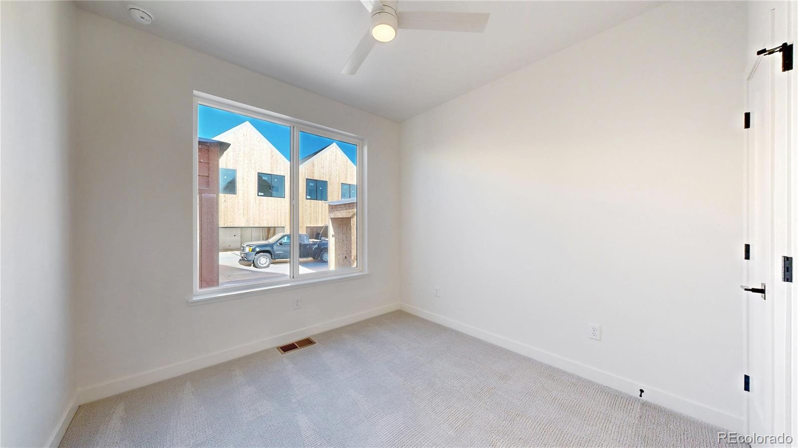 Empty carpeted bedroom with a wide window and ceiling fan.