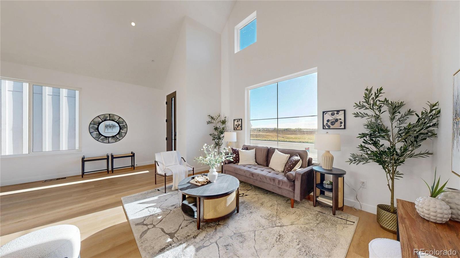 Staged living room with vaulted ceiling, large windows, and views across open land.