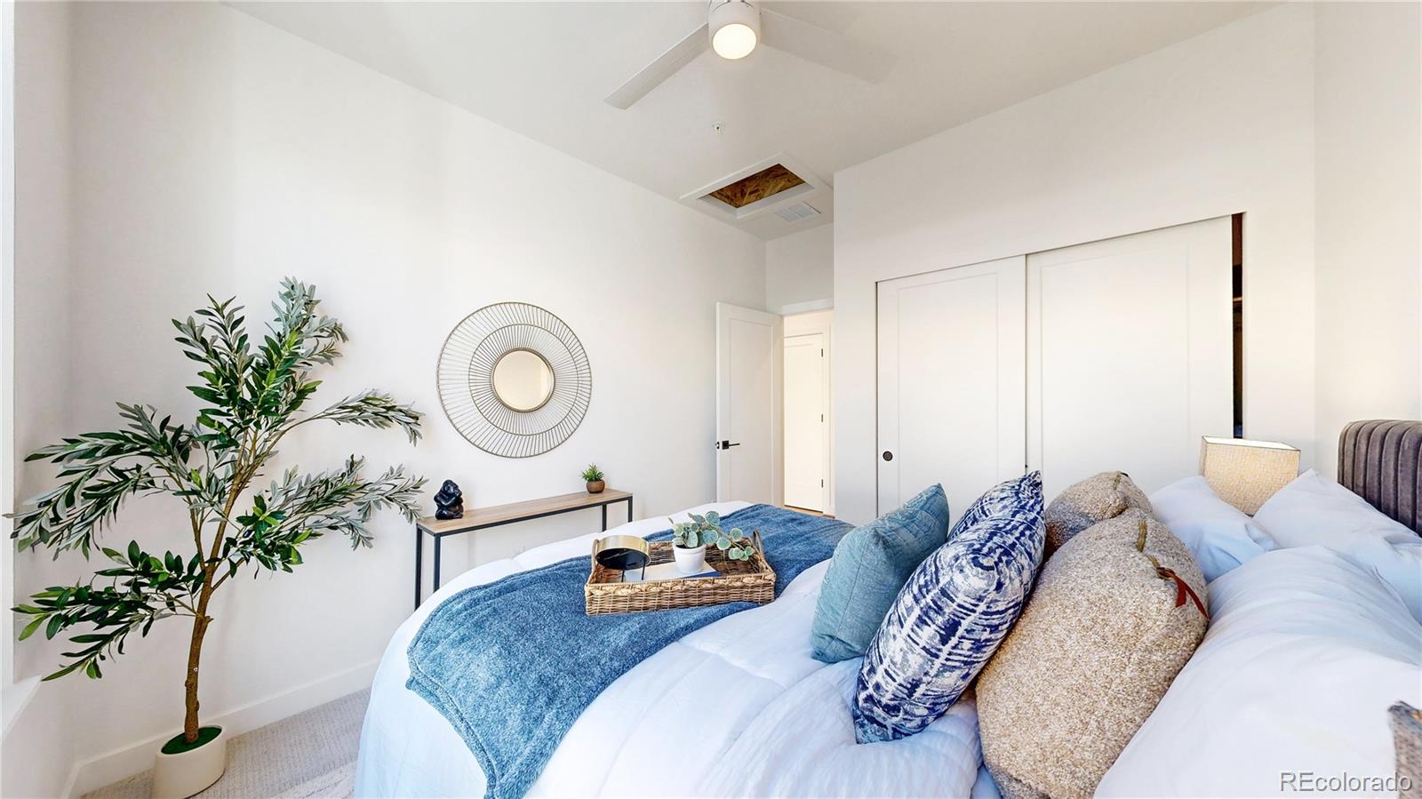 Staged bedroom with a white bed, blue throw, decorative pillows, and ceiling fan.