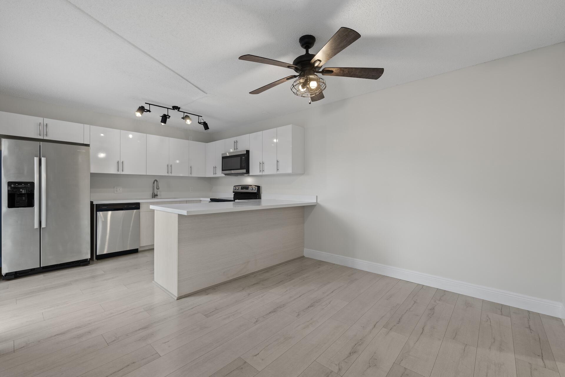 Unfurnished kitchen with white cabinets, a large peninsula, stainless steel appliances, and pale plank flooring.