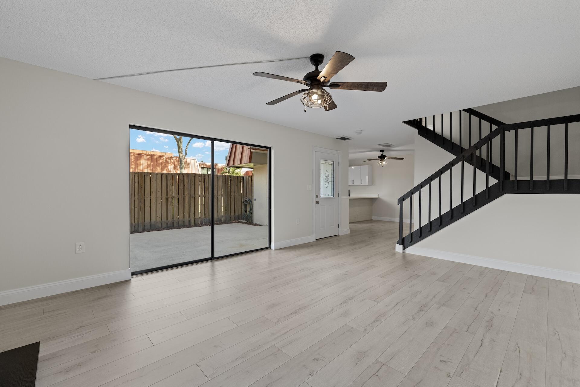 Unfurnished living room with pale flooring, a black staircase, and sliding glass doors to a fenced patio.