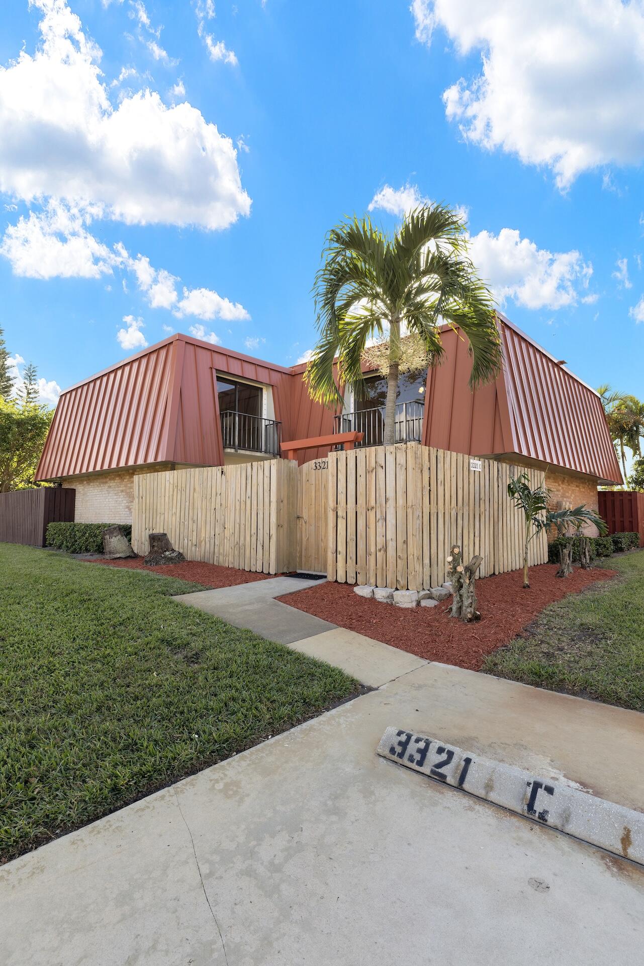 Two-story home with red metal siding, a wooden privacy fence, and a palm tree.