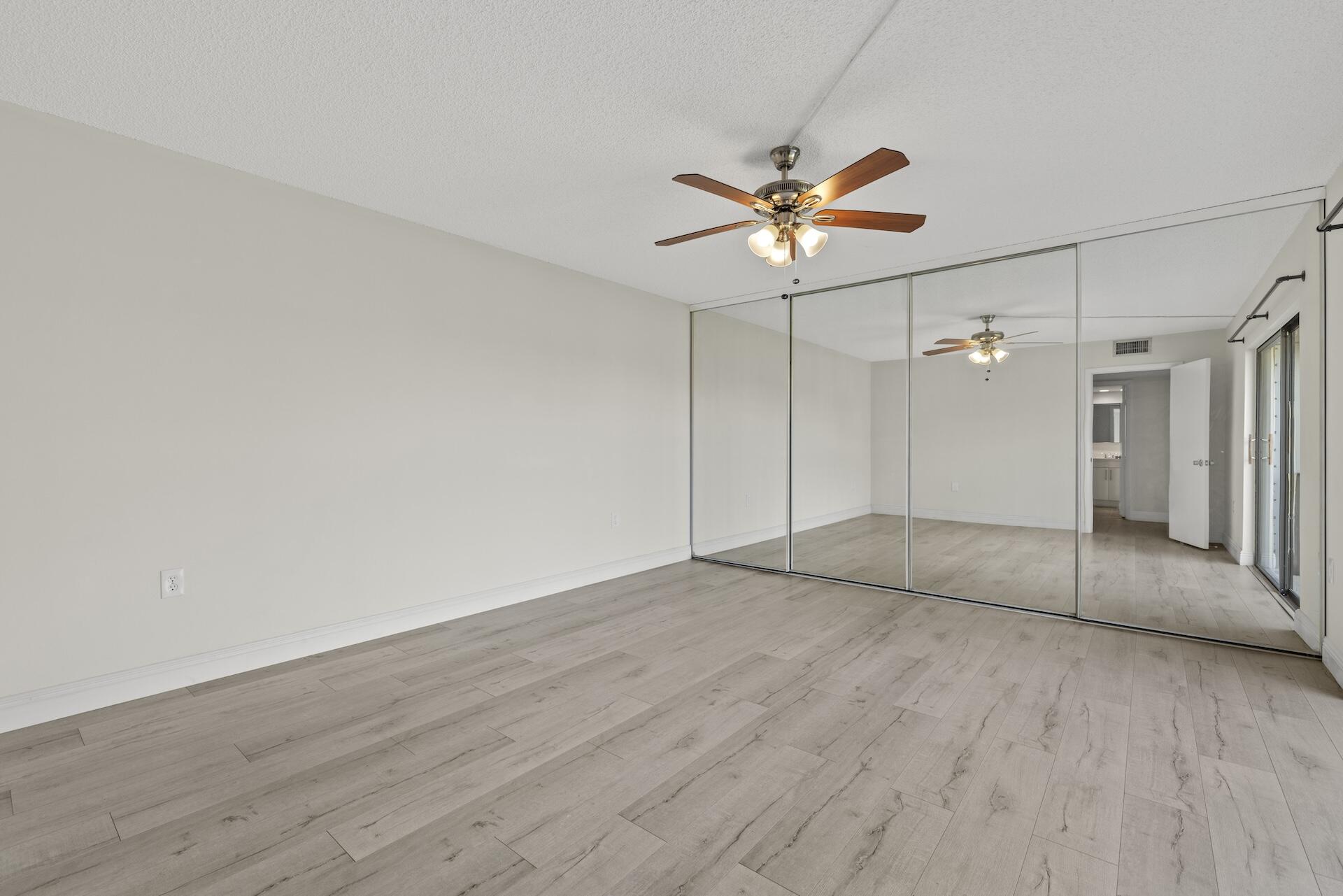 Empty bedroom with mirrored closet doors, light wood-look flooring, and a ceiling fan.