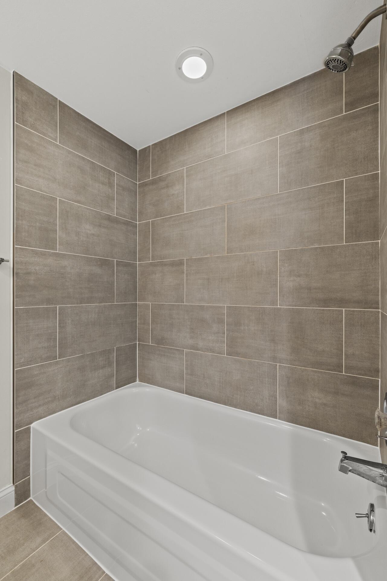 Bathroom bathtub with taupe tiled walls and a chrome showerhead.