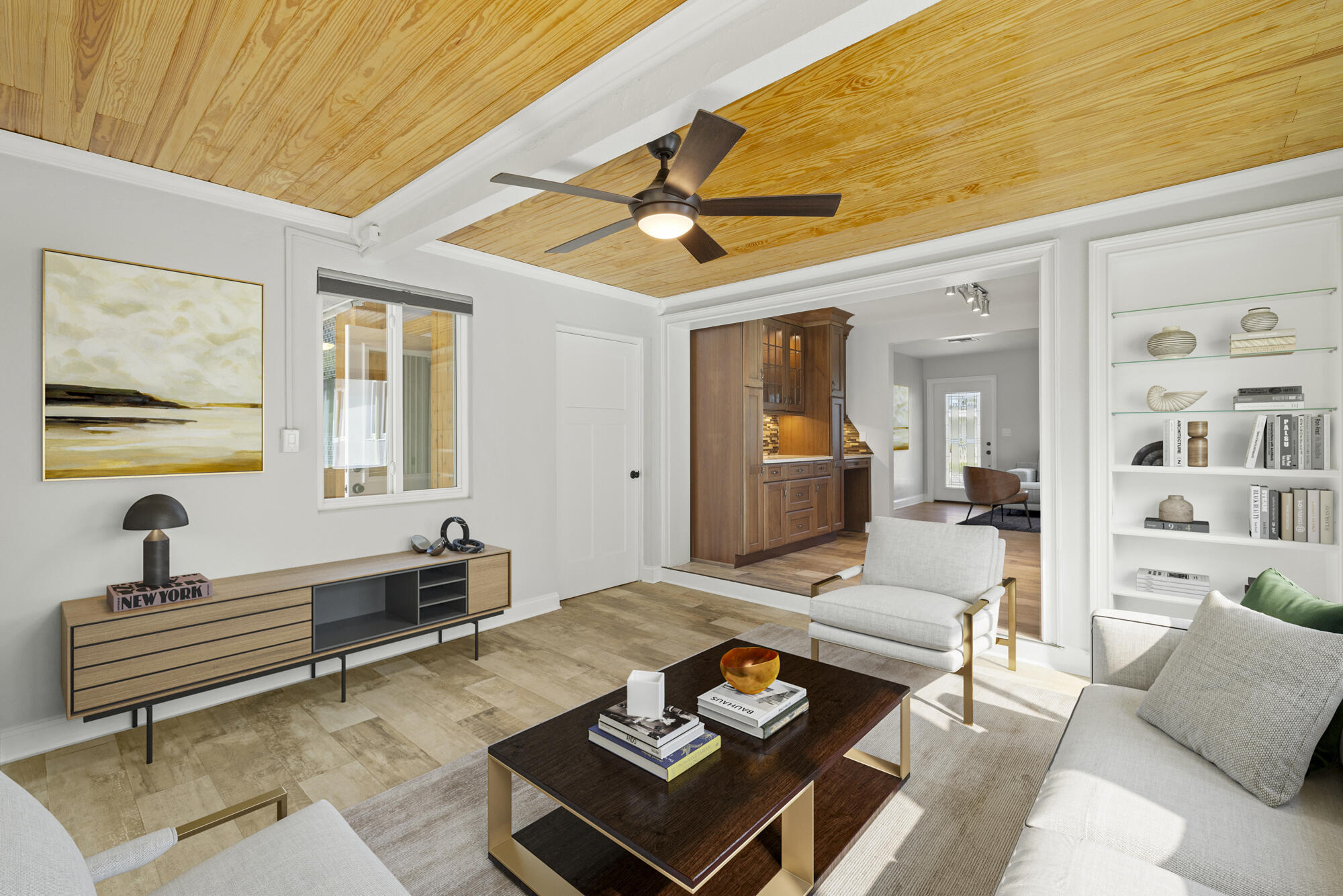 Living room with a wood-paneled ceiling, built-in shelves, and an open view into the kitchen.