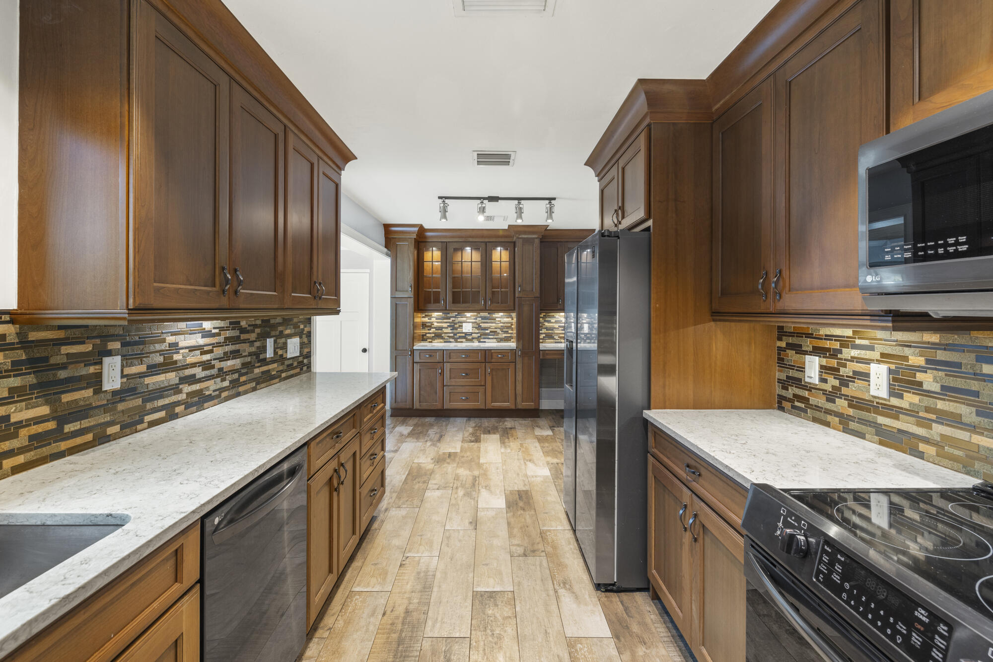 Galley kitchen with dark wood cabinets, white countertops, patterned tile backsplashes, and stainless steel appliances.