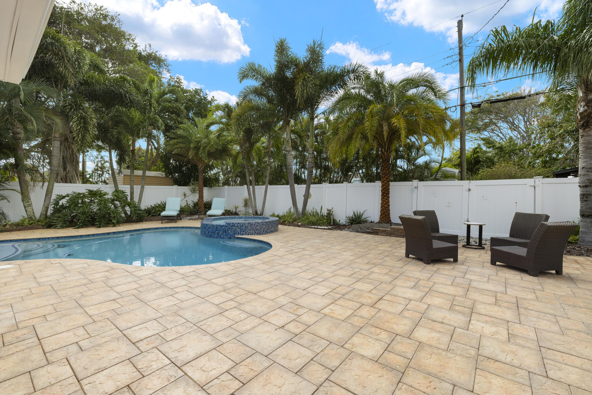 Backyard pool and raised spa on a stone patio, surrounded by palms and white fencing.