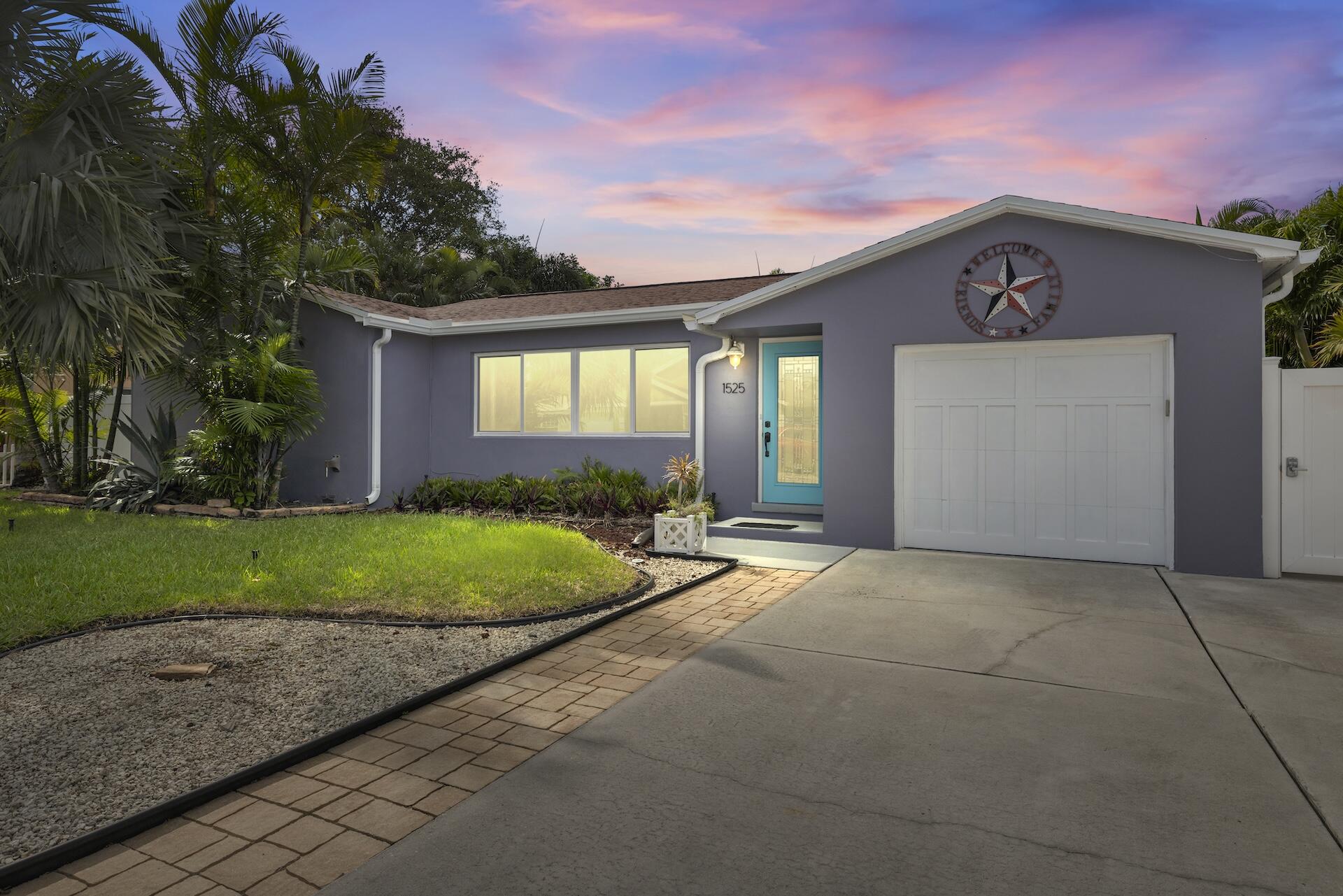 Purple single-story home with a turquoise entry door, white garage, and tropical landscaping at dusk.