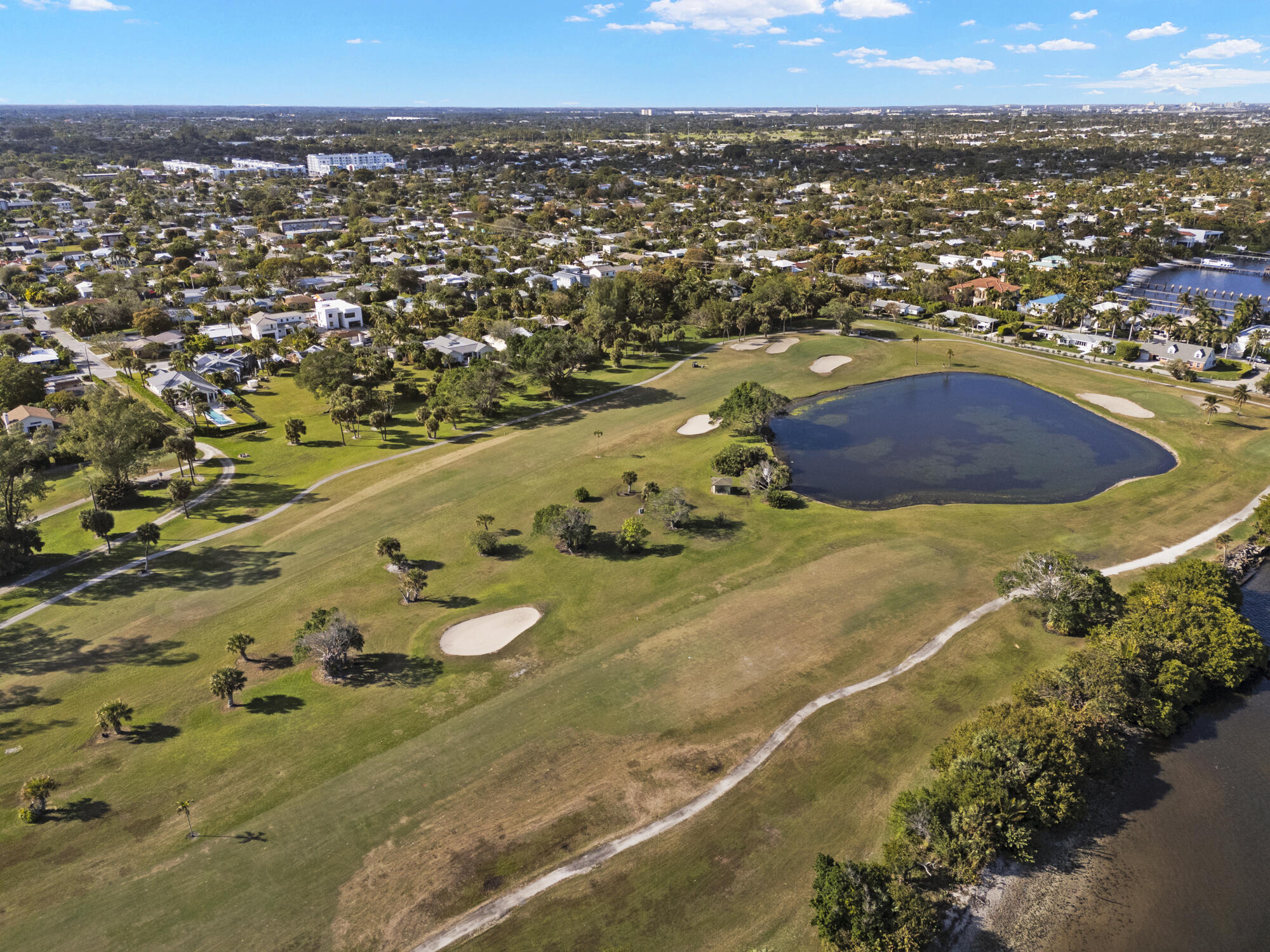 Aerial view of a golf course with sand bunkers and a pond beside a residential neighborhood.