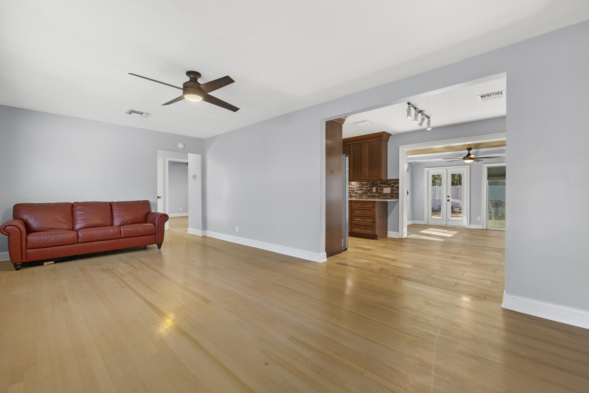 Living room with wood floors, a leather sofa, and an open view into the kitchen and dining area.