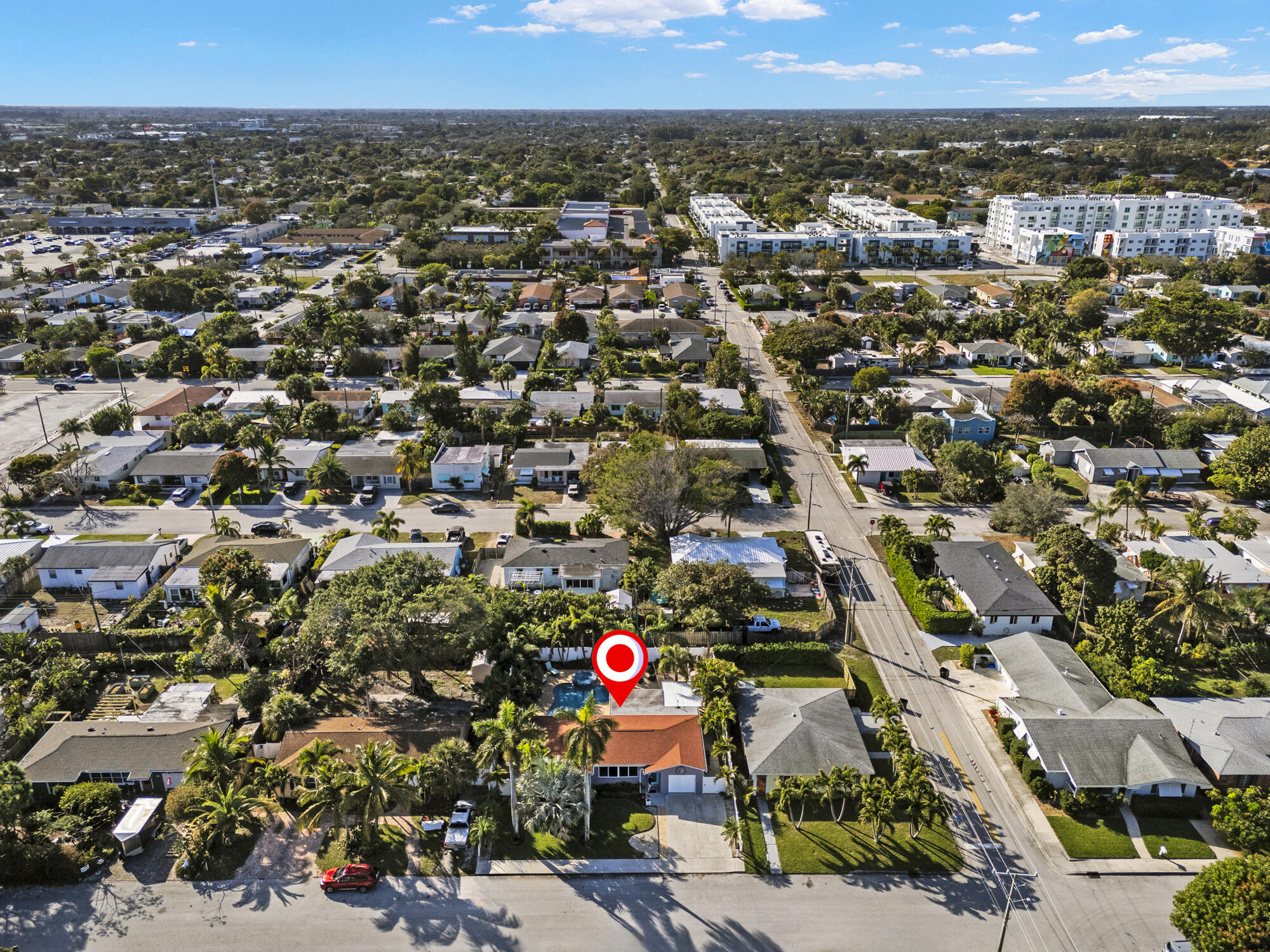 Aerial view of a red-roofed home marked by a red location pin among palm-lined neighborhood streets.