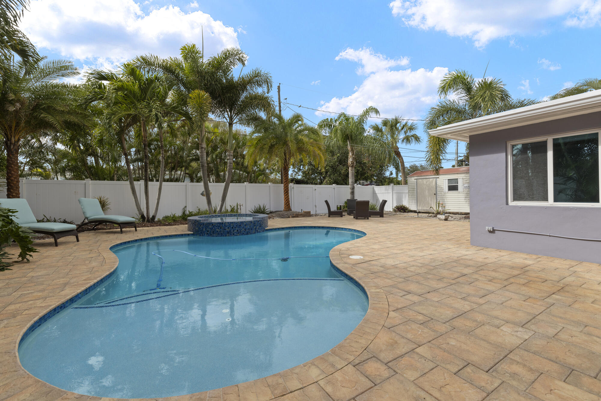 Backyard swimming pool with a raised tiled spa, palm trees, and a broad stone-paver deck.