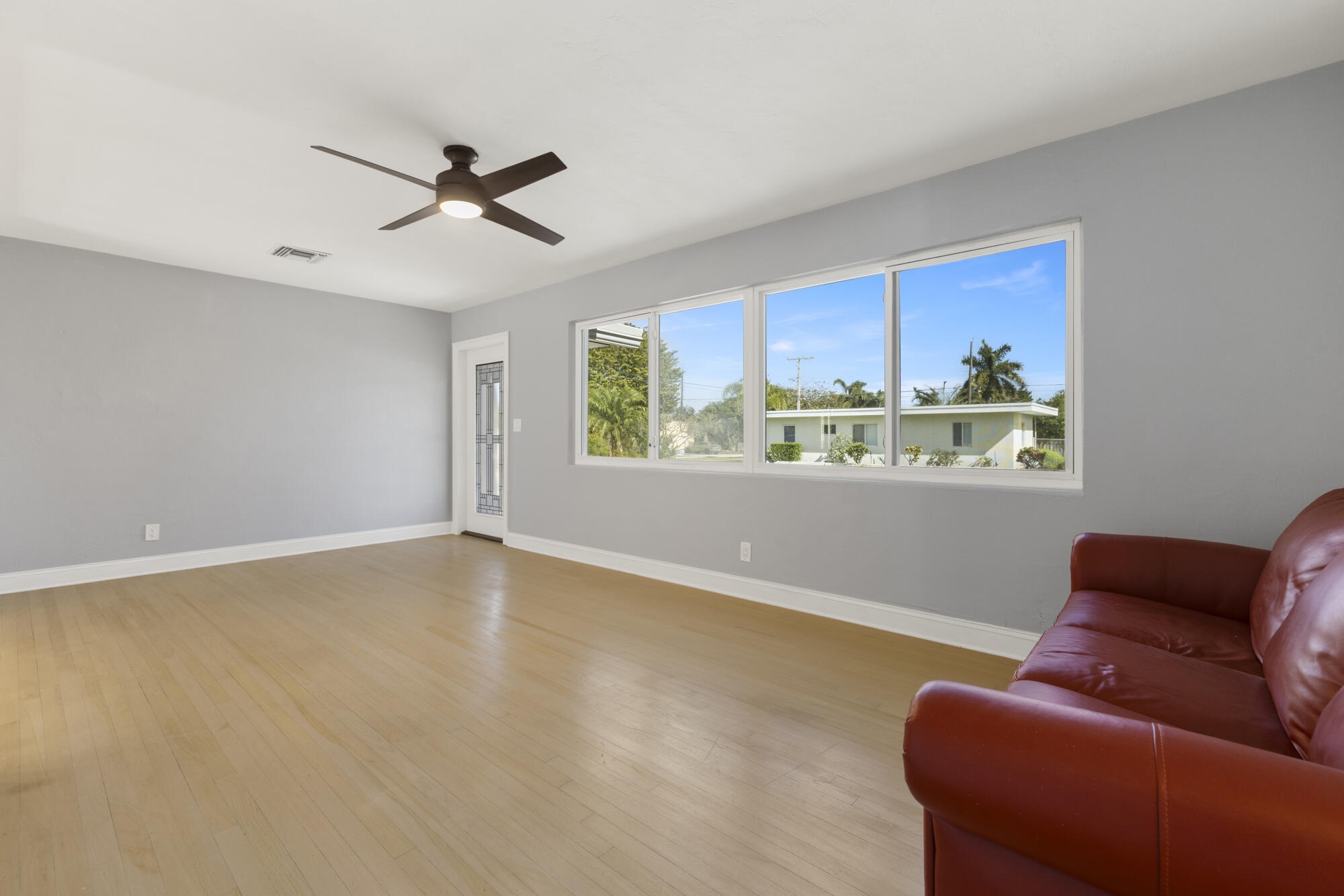 Living room with light wood floors, a large window, and a red leather sofa.