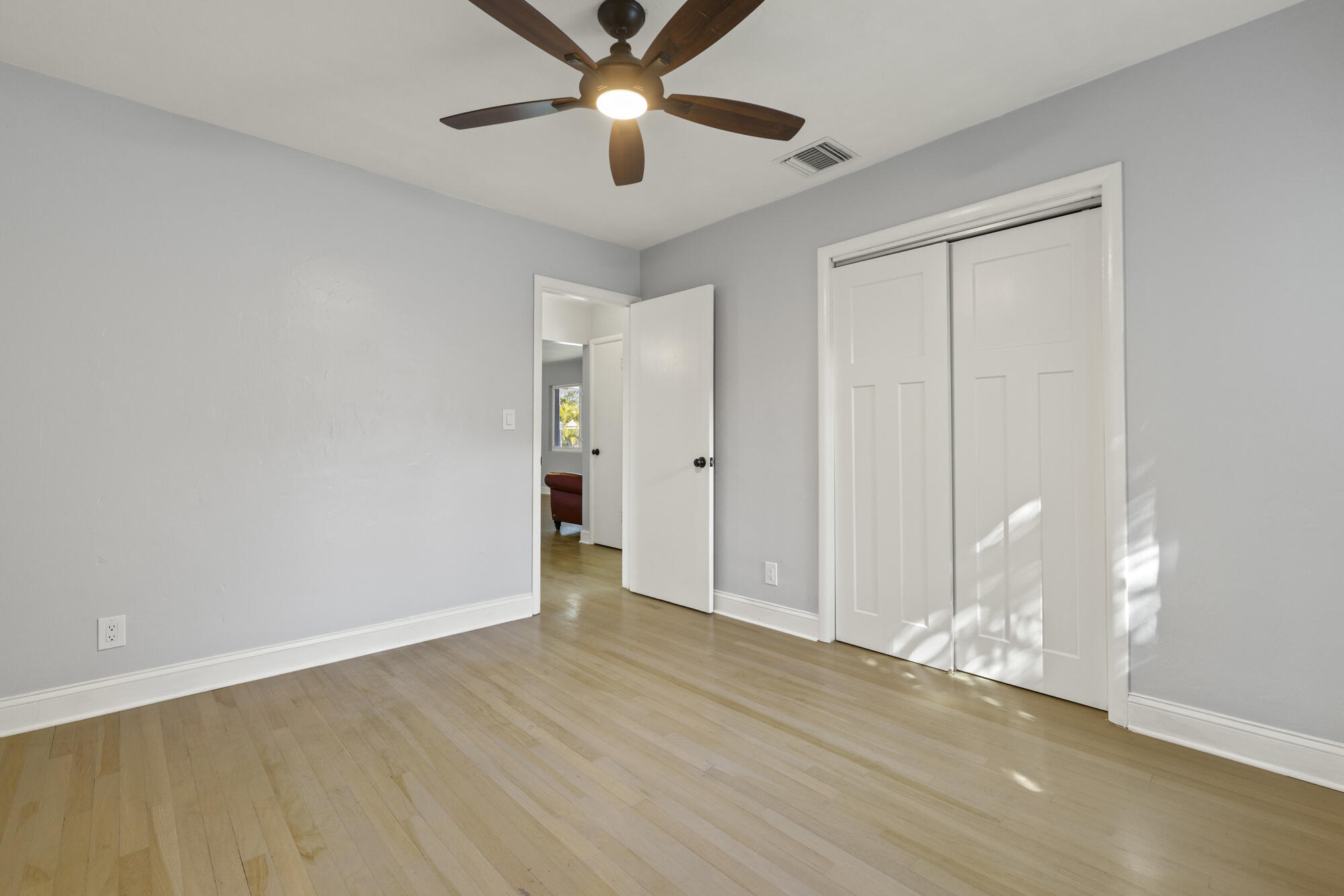 Empty bedroom with light wood floors, a ceiling fan, and white sliding closet doors.