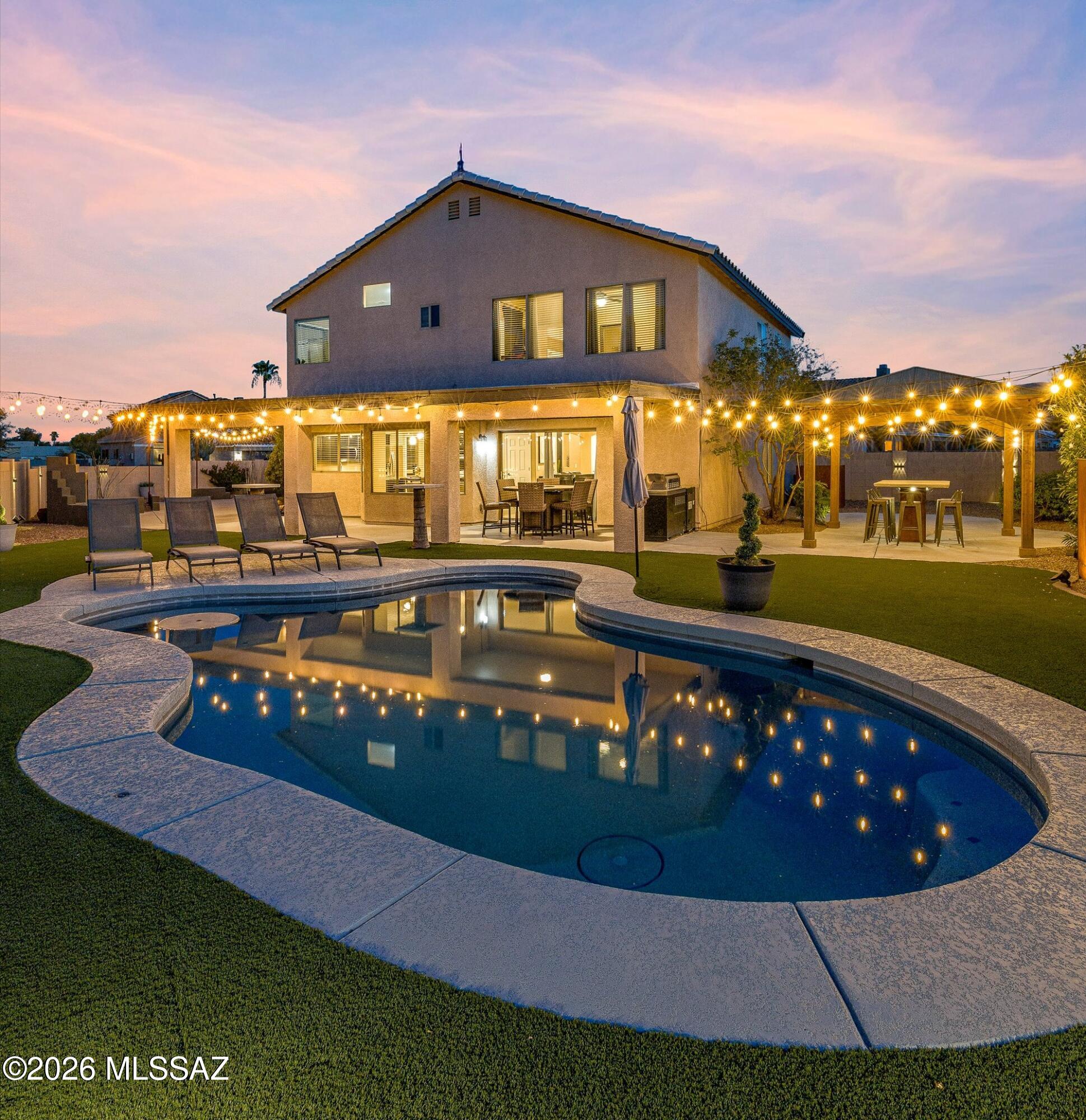 Two-story home and curving swimming pool at dusk, with glowing patio string lights.