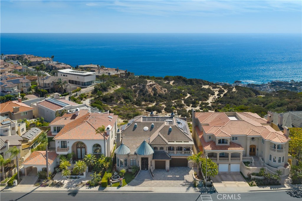 Coastal homes with terracotta roofs overlook scrub-covered hills and the Pacific Ocean.