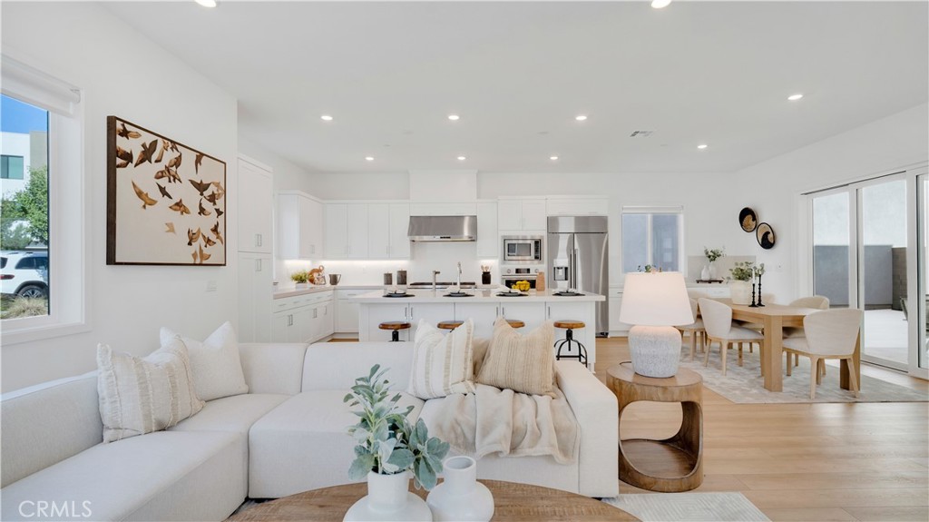 Open-plan living room, kitchen, and dining area with white furnishings and light wood floors.