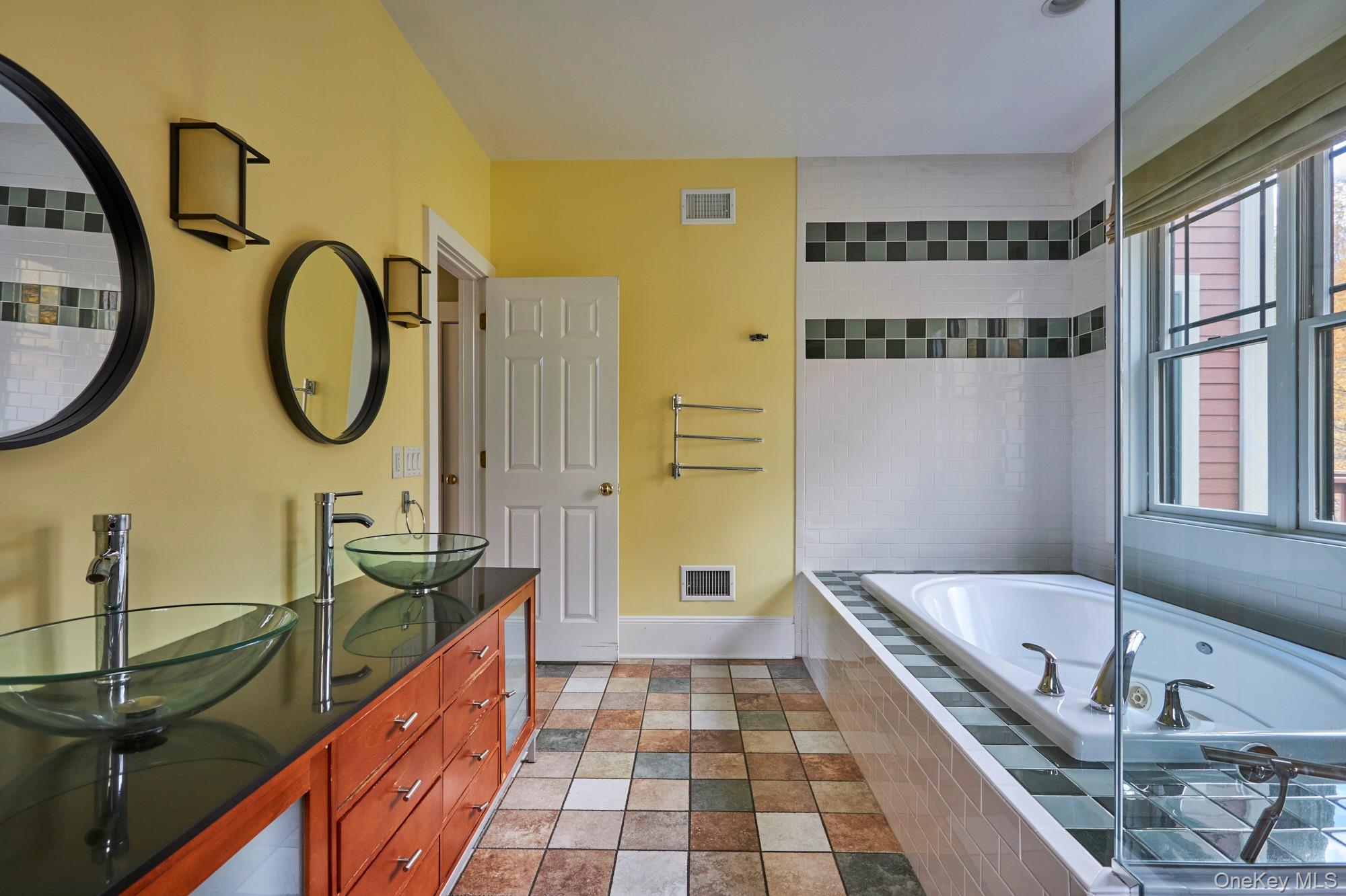 Bathroom with a soaking tub by large windows and a wood vanity with two glass vessel sinks.