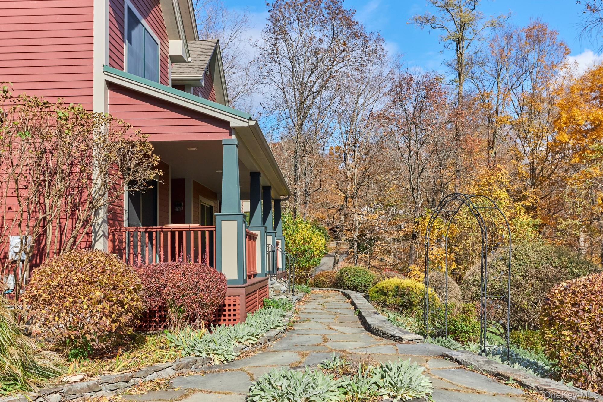 Red-sided home with a covered porch and stone walkway winding through autumn gardens.