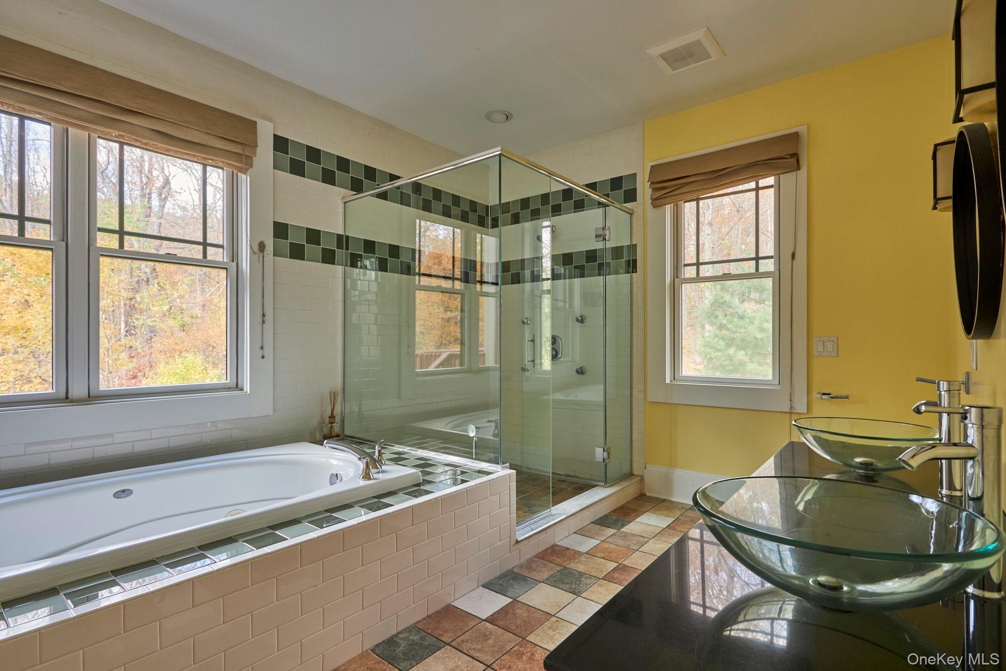 Bathroom with a glass shower, built-in soaking tub, and double glass vessel sinks.