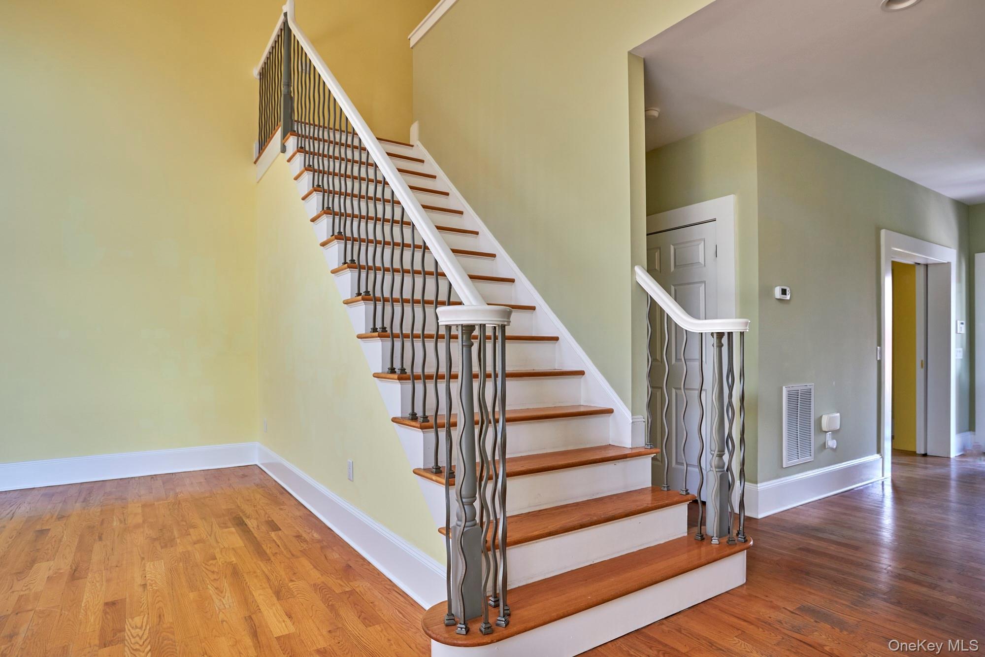Empty foyer with a wood-and-white staircase and dark wavy metal balusters.
