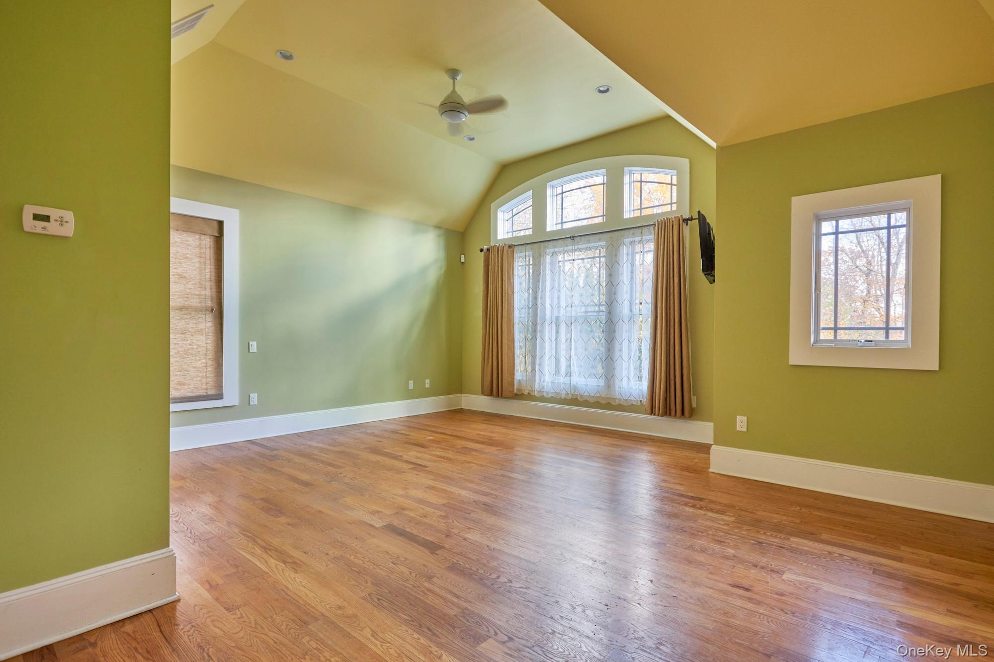 Empty room with green walls, hardwood floors, vaulted ceiling, and tall curtained windows.