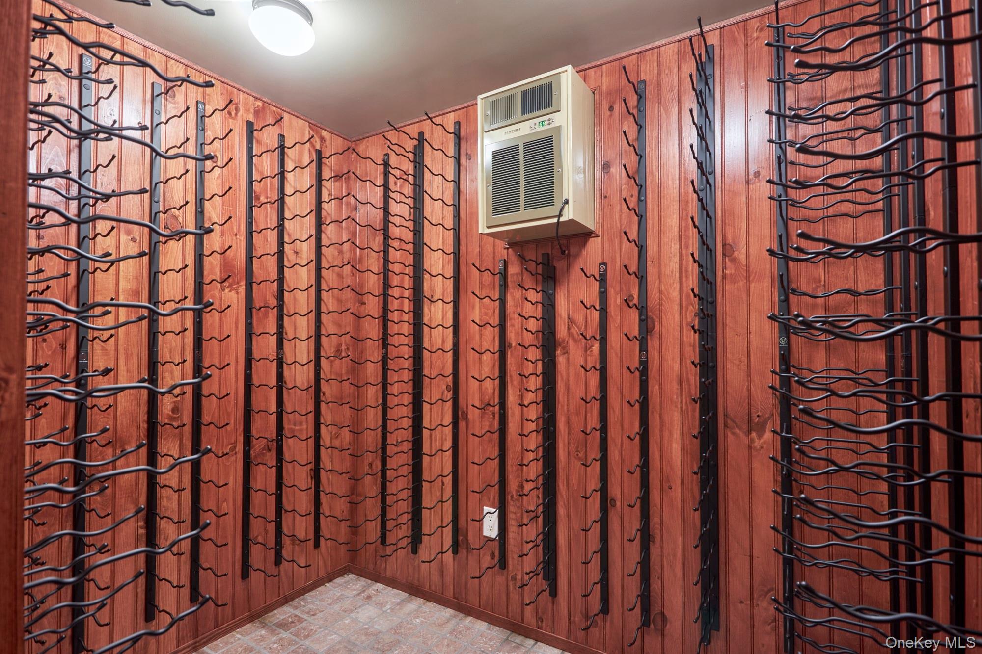 Wine cellar lined with wooden walls and black metal wine racks, with a wall-mounted climate-control unit.