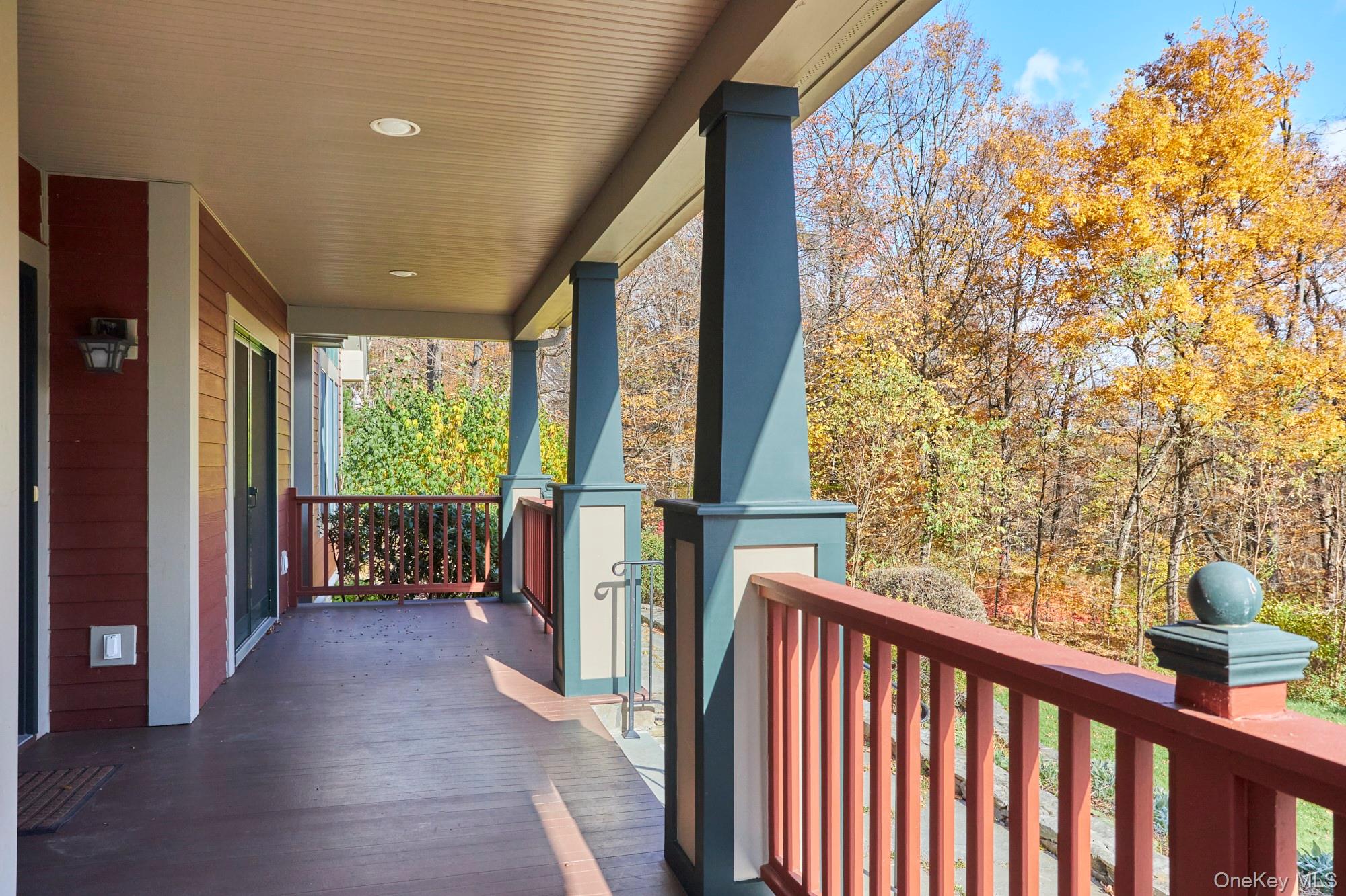 Covered porch with red railings and blue columns overlooking autumn trees.